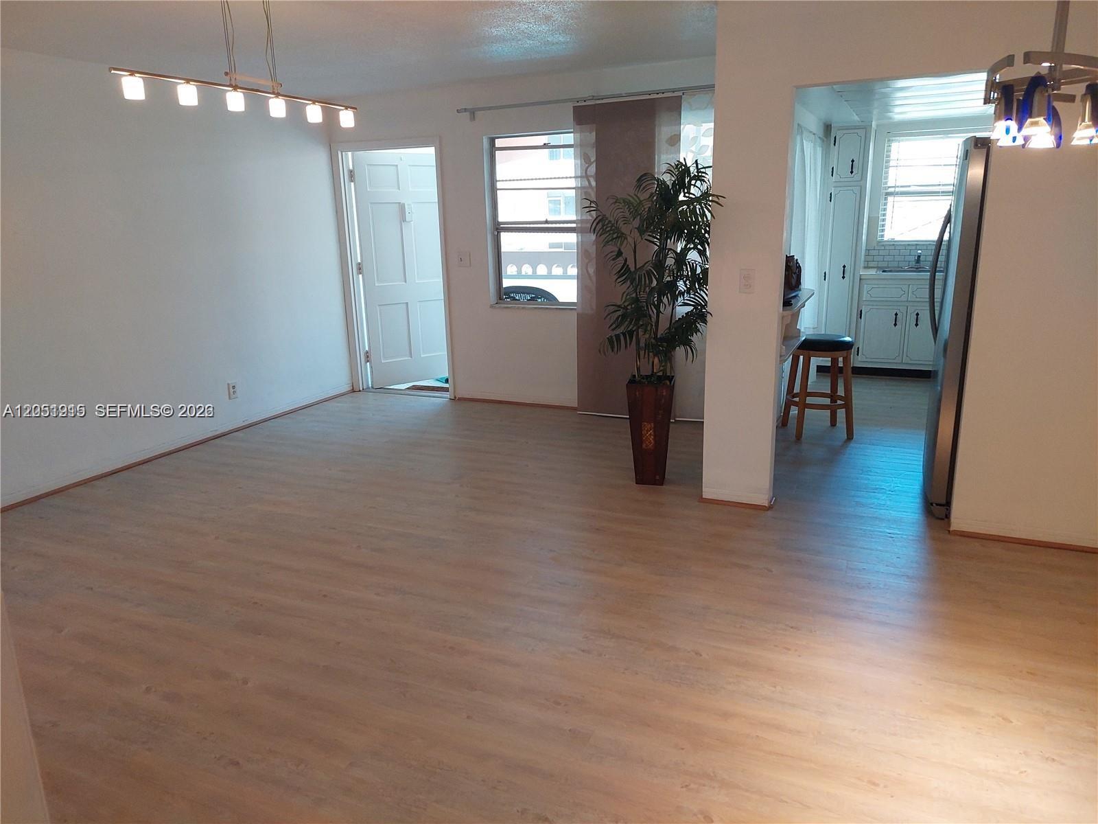 An open living area features light wood-look flooring, a ceiling light fixture, and a kitchen — 180 12 # 15c, Hallandale Beach FL 33009, HALLANDALE BEACH, FL