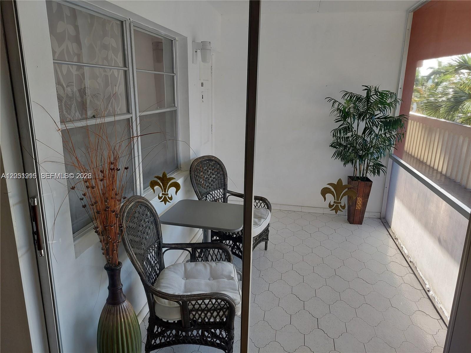 A covered balcony features wicker chairs, a small table, a potted plant, and tiled flooring — 180 12 # 15c, Hallandale Beach FL 33009, HALLANDALE BEACH, FL