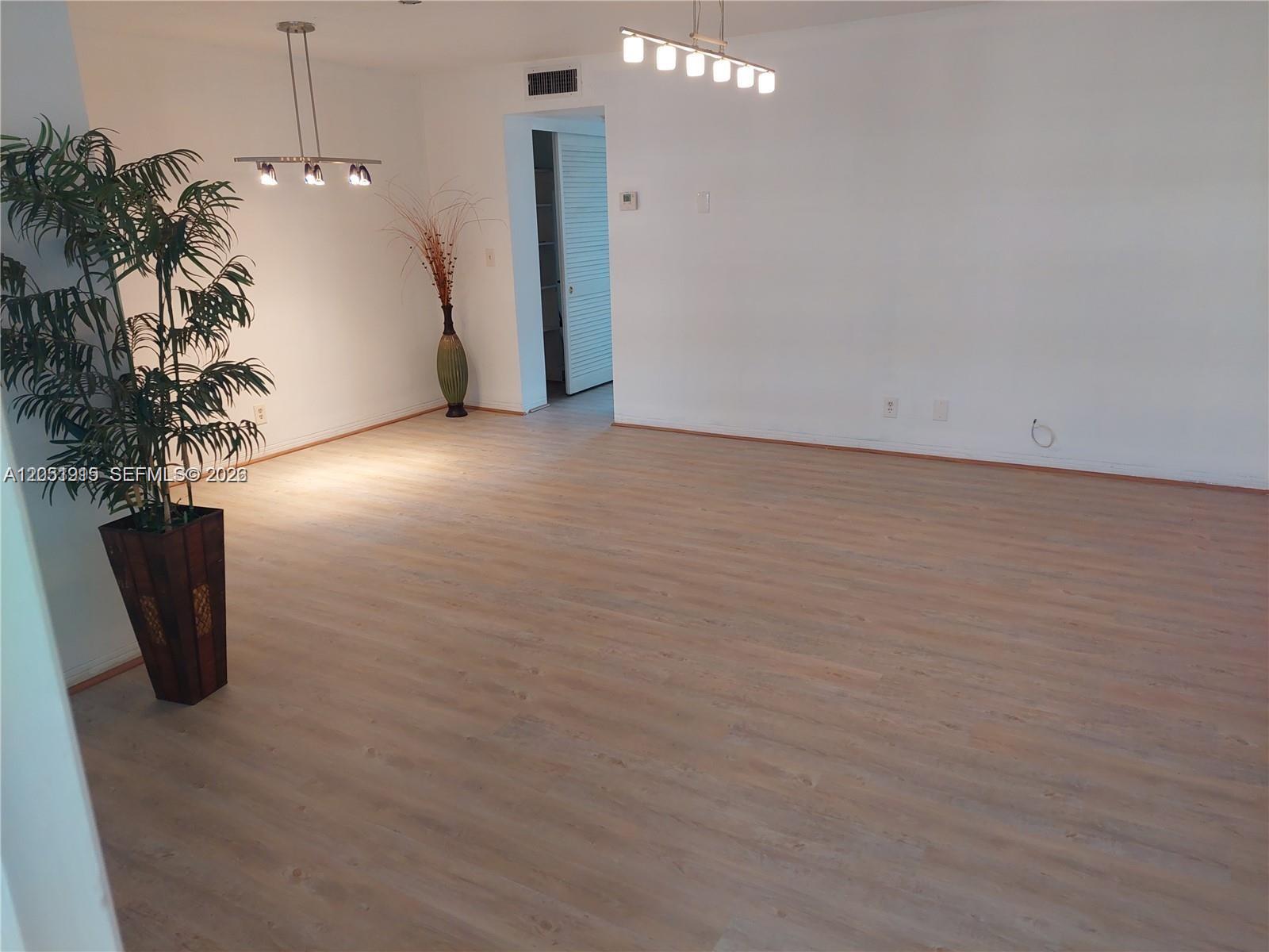 An empty room features light wood-look flooring, white walls, and two modern pendant light fixtures — 180 12 # 15c, Hallandale Beach FL 33009, HALLANDALE BEACH, FL
