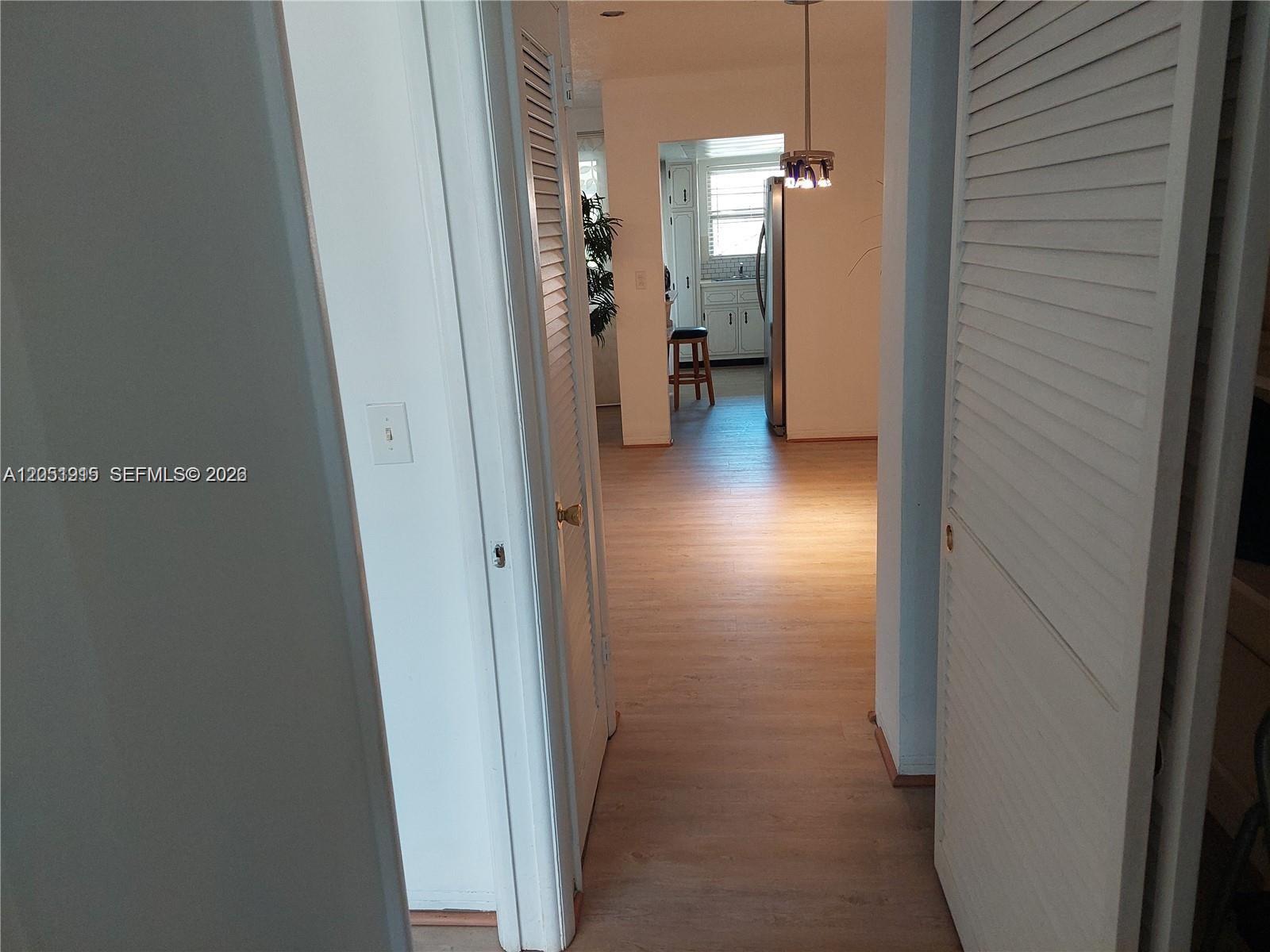 A hallway with light wood-look flooring leads to a kitchen with white cabinets — 180 12 # 15c, Hallandale Beach FL 33009, HALLANDALE BEACH, FL
