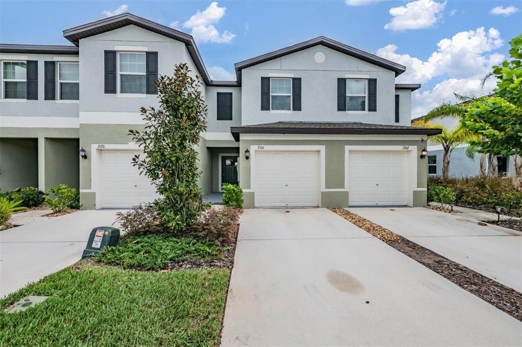A two-story townhouse exterior features three garage doors, light-colored stucco walls, and a small lawn — 2166 GREAT SAPPHIRE LANE, LUTZ, FL