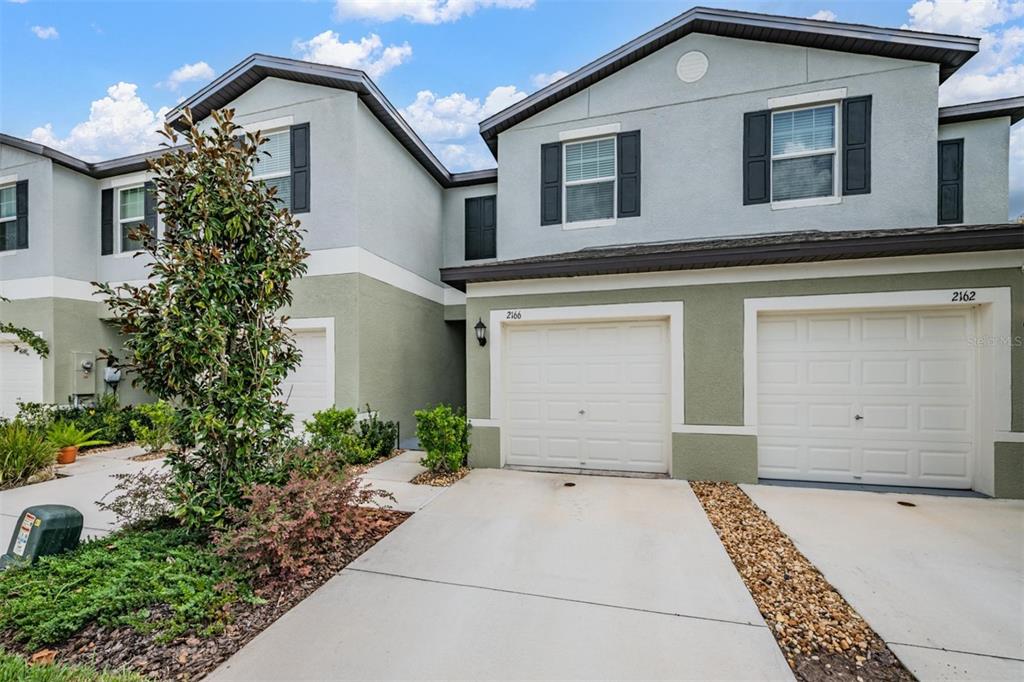 The exterior of two attached townhomes features light-colored stucco, dark shutters, and white garage doors — 2166 GREAT SAPPHIRE LANE, LUTZ, FL