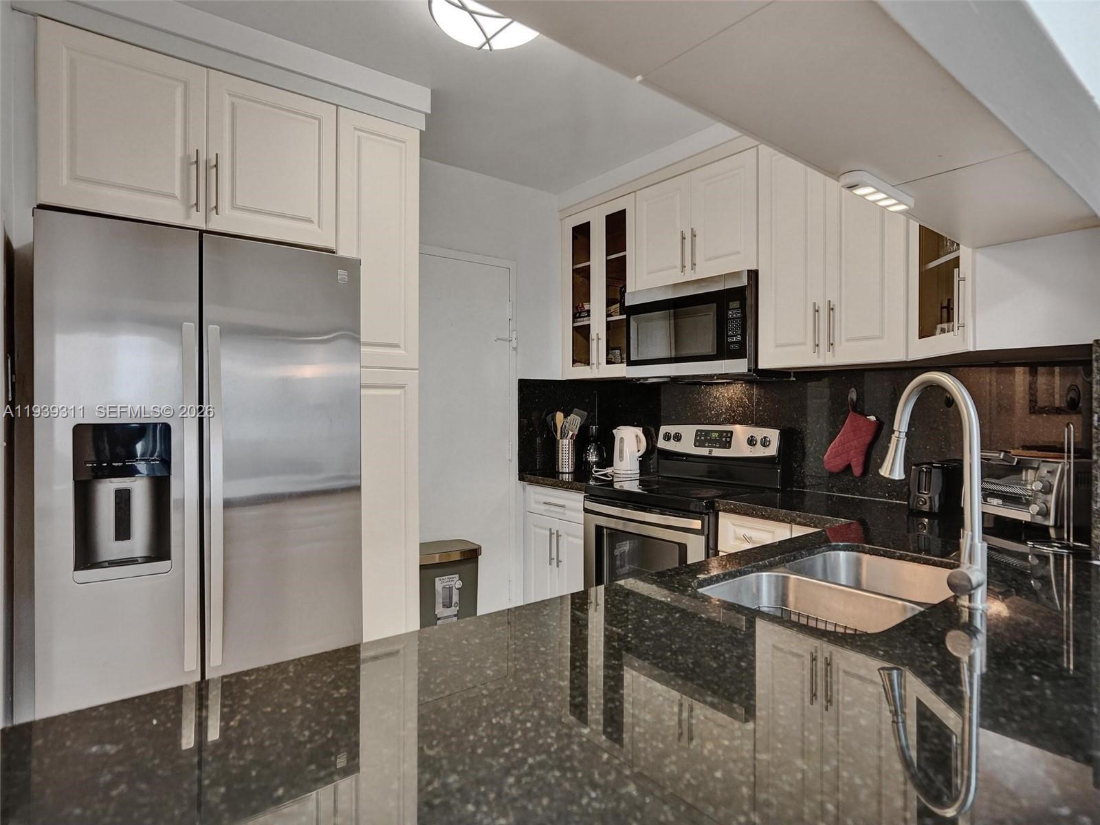 A kitchen features white cabinets, black granite countertops, stainless steel appliances, and a double sink — 3725 S Ocean Dr # 520, Hollywood FL 33019, HOLLYWOOD, FL
