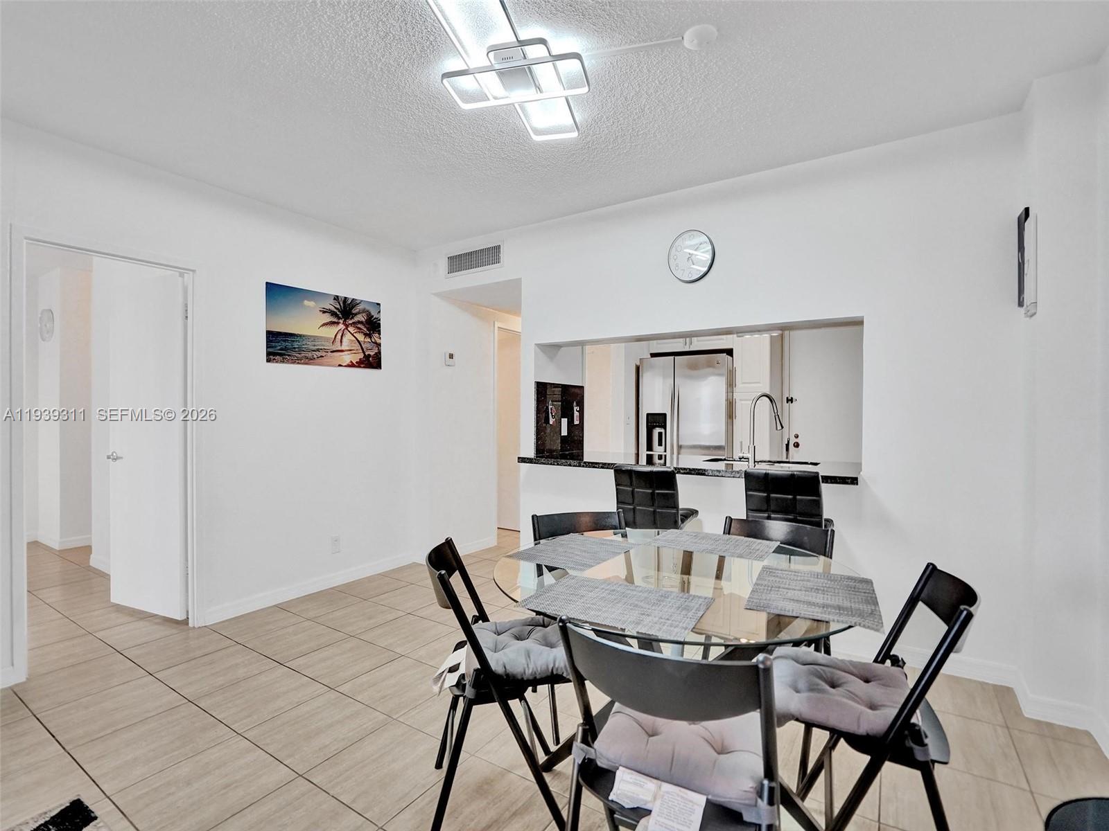 A dining area with a glass table and chairs sits in front of a kitchen pass-through — 3725 S Ocean Dr # 520, Hollywood FL 33019, HOLLYWOOD, FL