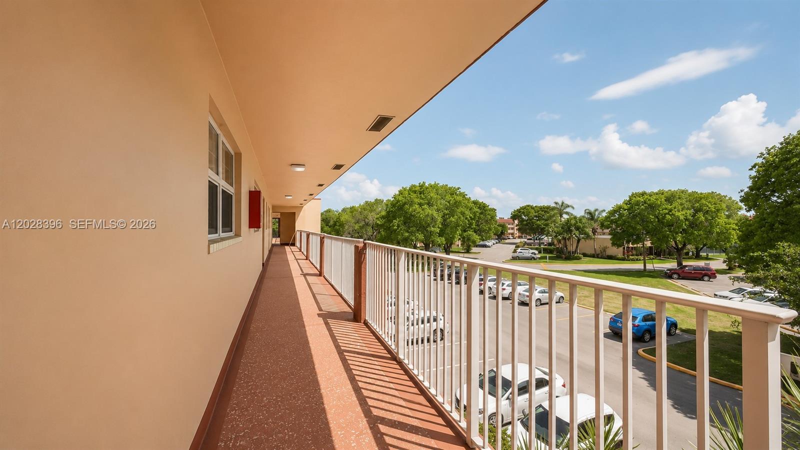 An outdoor walkway with a white railing overlooks a parking lot and green trees — 2811 N Pine Island Rd # 302, Sunrise FL 33322, SUNRISE, FL