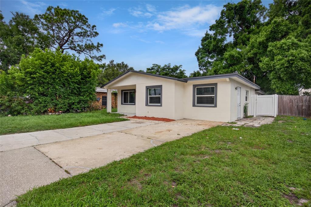 A single-story house with a concrete driveway, white stucco exterior, and dark-framed windows — 1610 N LOIS AVENUE, TAMPA, FL