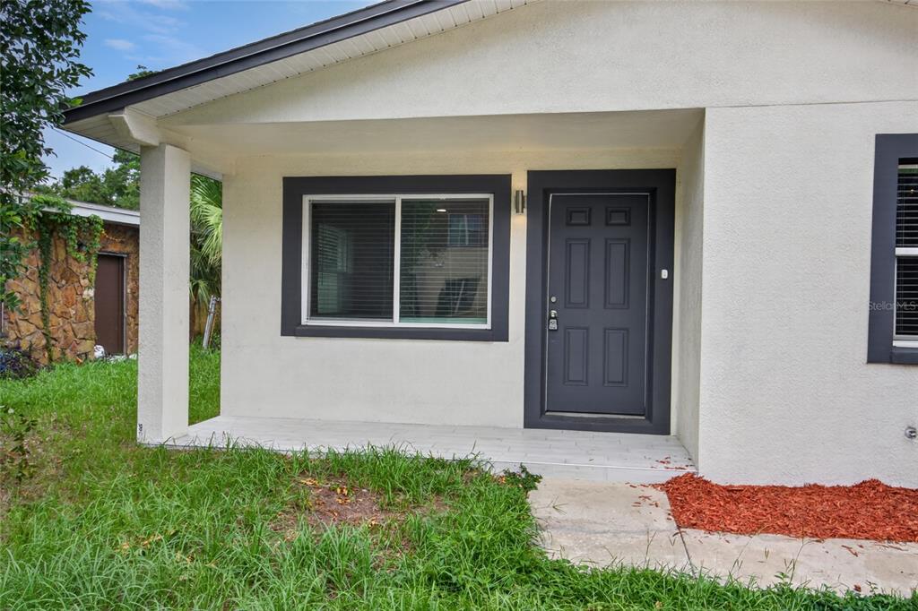 The exterior of a house features a covered porch, a dark gray front door, and windows — 1610 N LOIS AVENUE, TAMPA, FL