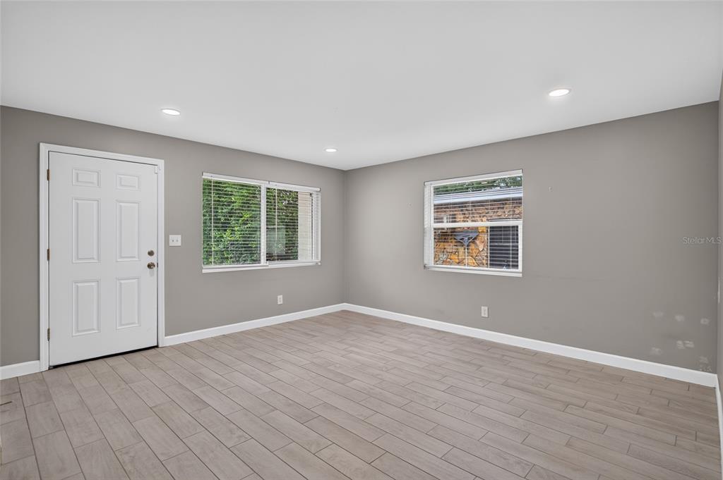 An empty room features gray walls, light wood-look tile flooring, two windows, and a white door — 1610 N LOIS AVENUE, TAMPA, FL