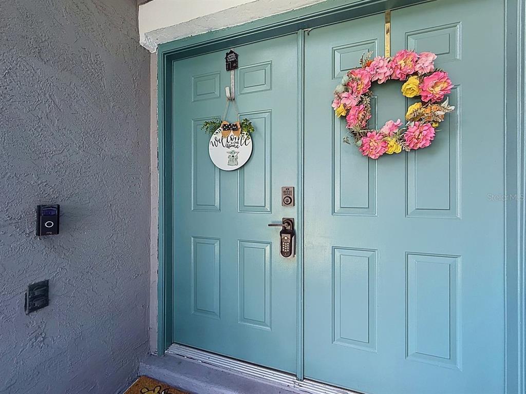 A teal double front door features a floral wreath, a small sign, and a smart lock — 527 DOMINISH ESTATES DRIVE, APOPKA, FL