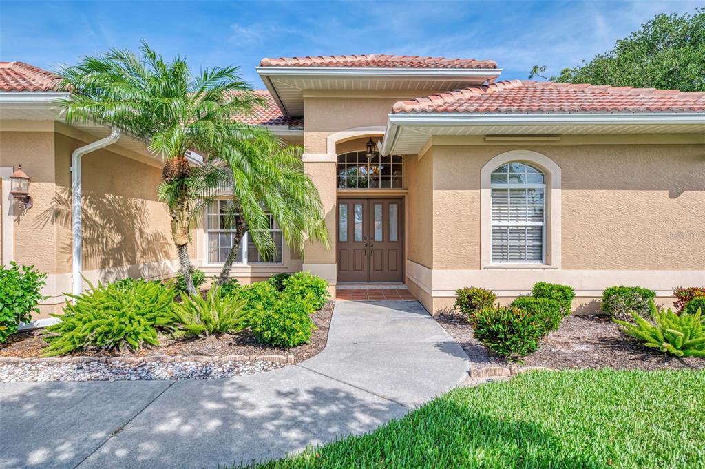A tan stucco house with a tiled roof, double front doors, and a palm tree — 763 EGRET WALK LANE, VENICE, FL