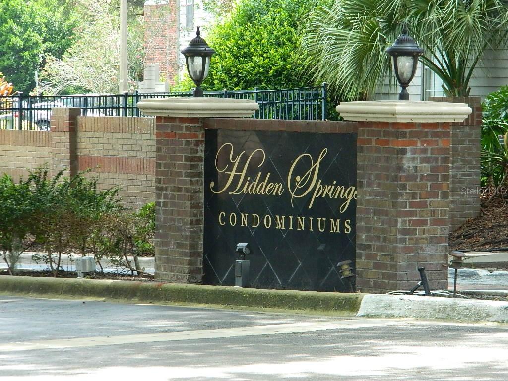 A brick entrance sign for Hidden Spring Condominiums features two lamps and decorative landscaping — 672 ROARING DRIVE UNIT 245, ALTAMONTE SPRINGS, FL