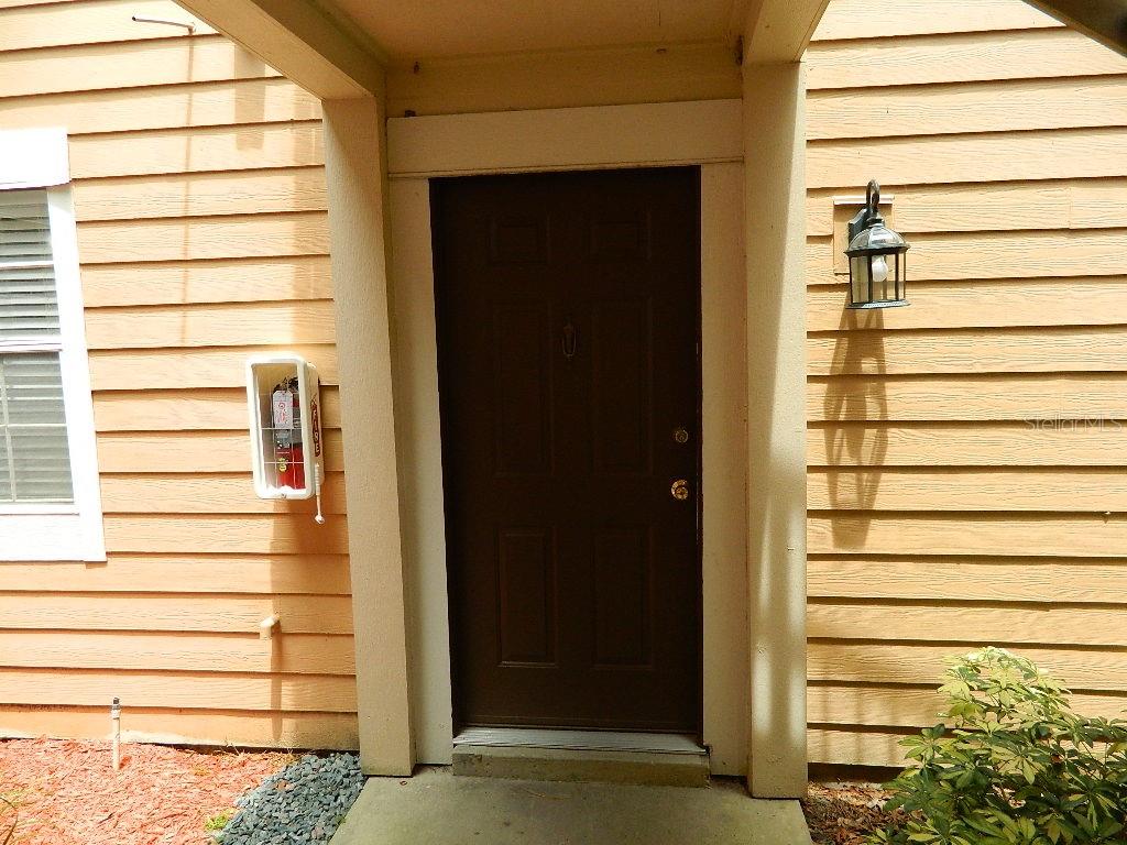 A dark brown front door is centered on a tan-sided exterior wall with a fire extinguisher — 672 ROARING DRIVE UNIT 245, ALTAMONTE SPRINGS, FL