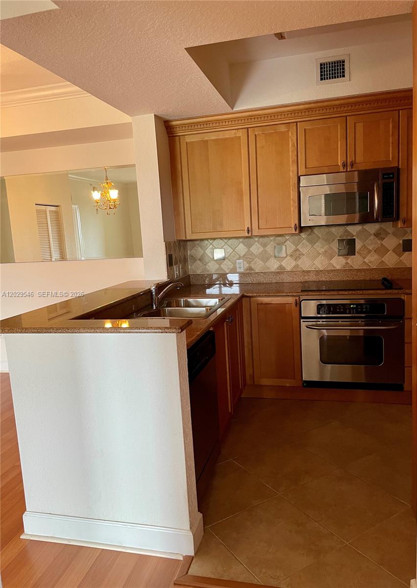 A kitchen features light wood cabinets, stainless steel appliances, and a granite countertop peninsula — 4408 Renaissance Way # 408, Boynton Beach FL 33426, BOYNTON BEACH, FL
