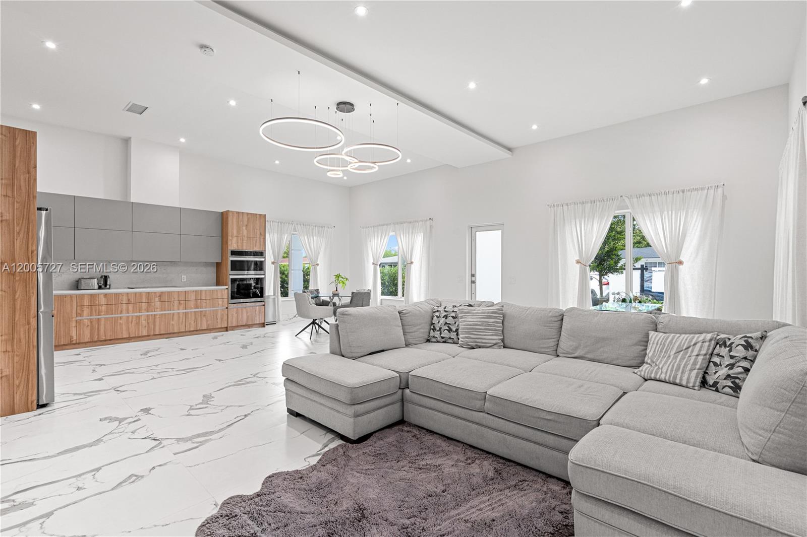 An open-concept living room and kitchen feature marble floors, a grey sectional, and modern lighting — 635 SW 9th St, Hallandale Beach FL 33009, HALLANDALE BEACH, FL