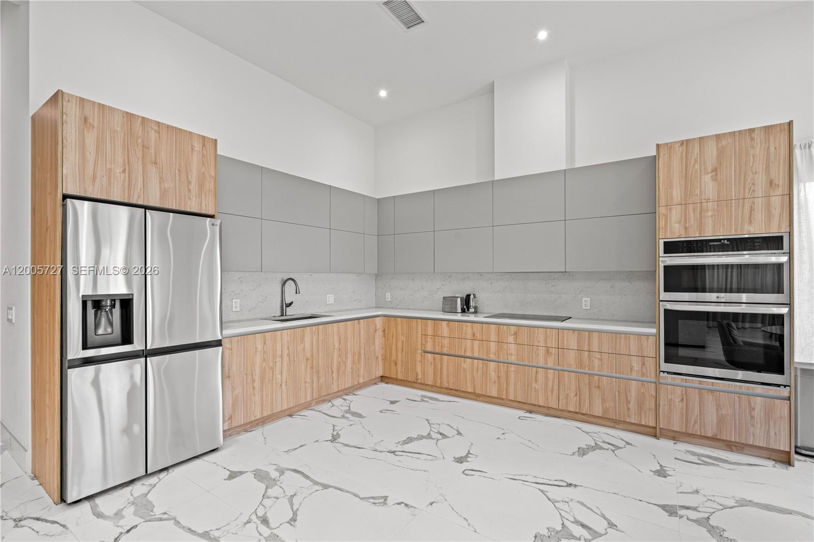 A modern kitchen features wood-grain cabinets, grey upper cabinets, stainless steel appliances, and marble flooring — 635 SW 9th St, Hallandale Beach FL 33009, HALLANDALE BEACH, FL