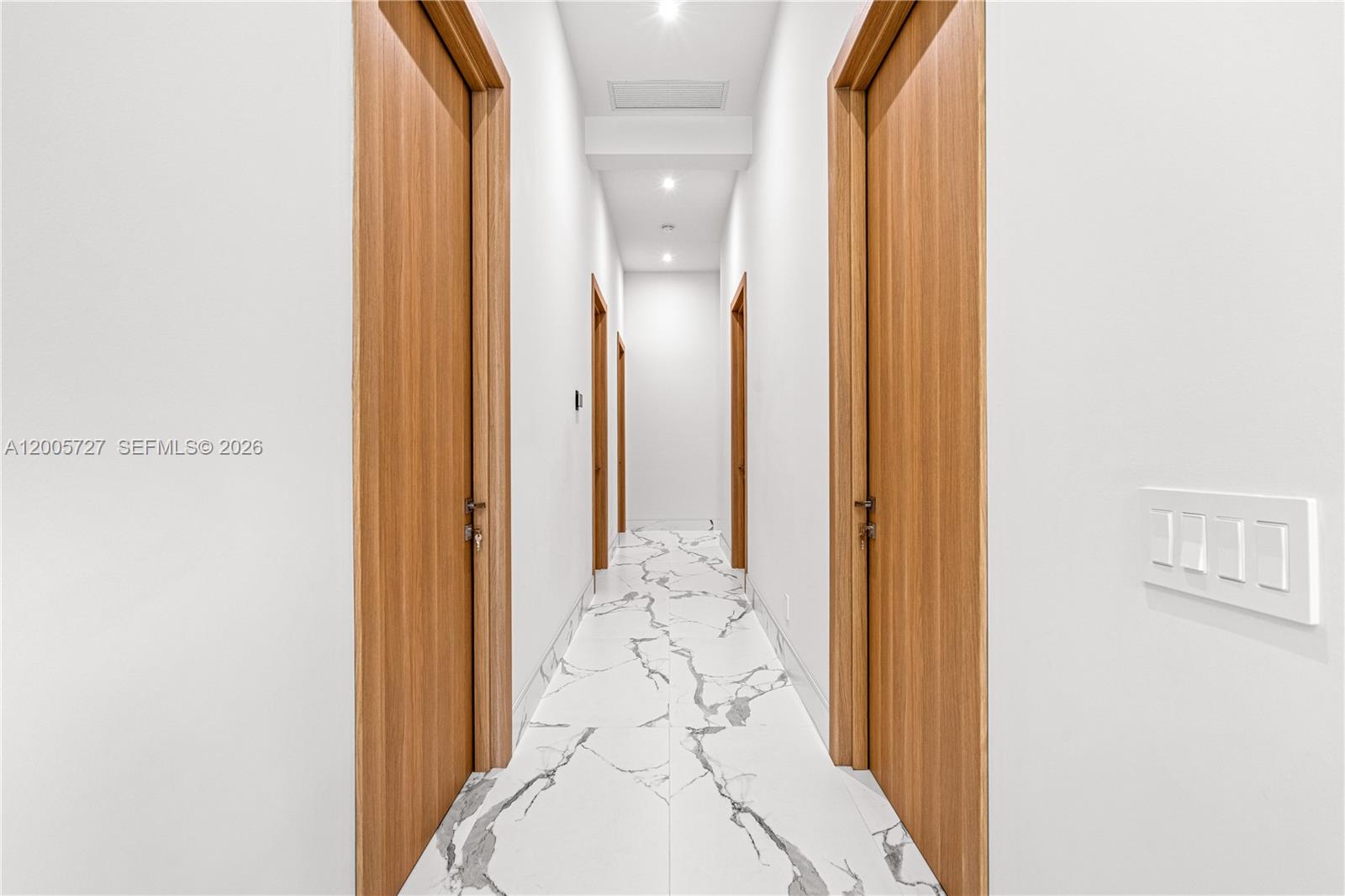 A narrow hallway features white marble flooring, plain white walls, and several wooden doors — 635 SW 9th St, Hallandale Beach FL 33009, HALLANDALE BEACH, FL