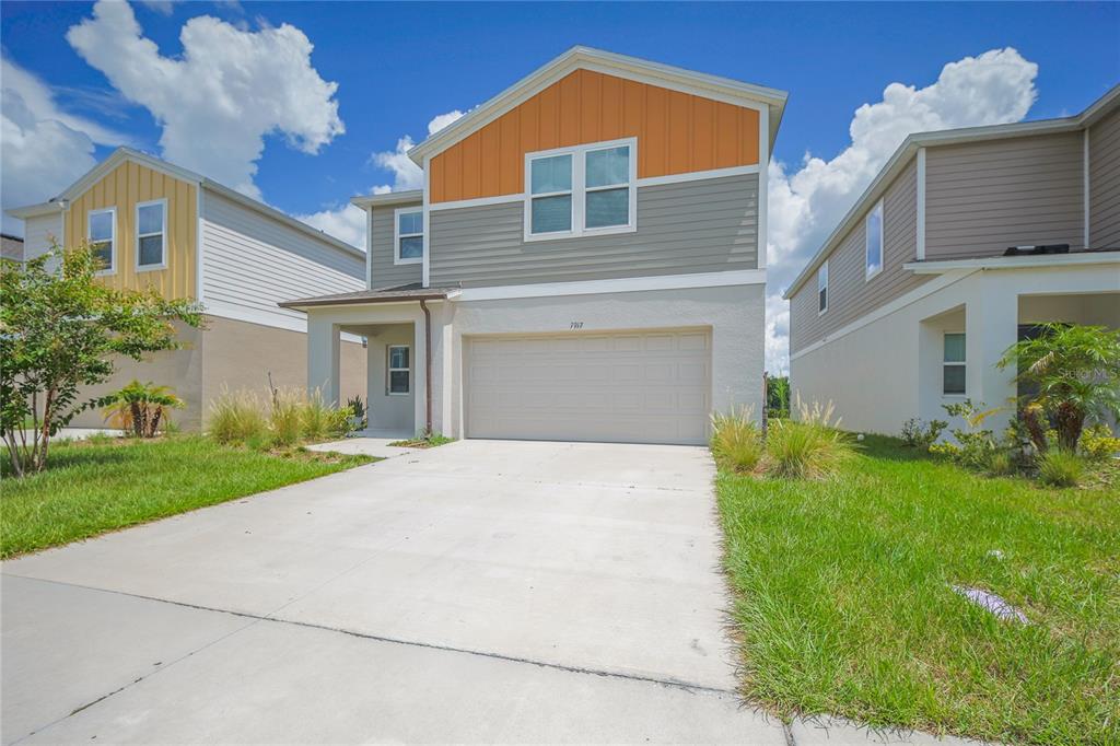 A two-story suburban house with a two-car garage, gray siding, and an orange gable — 7917 PEACE LILY AVENUE, WESLEY CHAPEL, FL