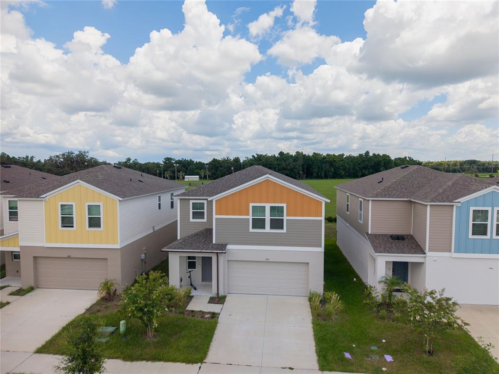 An aerial view shows three suburban two-story houses with garages and colorful siding — 7917 PEACE LILY AVENUE, WESLEY CHAPEL, FL