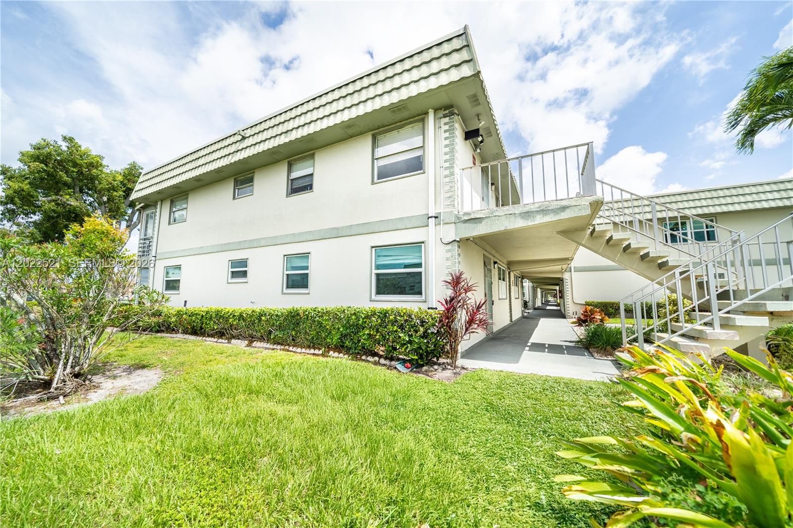 A two-story apartment building features a concrete staircase leading to an upper-level walkway — 145 Brittany D # 145, Delray Beach FL 33446, DELRAY BEACH, FL