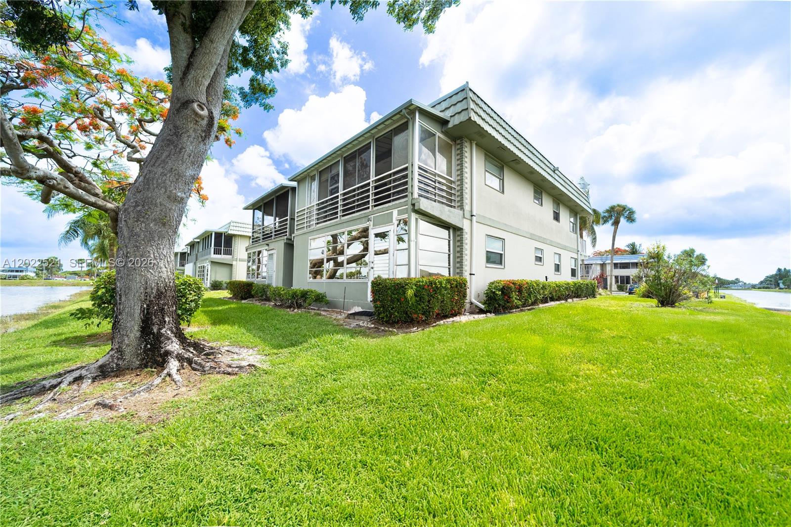 A two-story apartment building with screened balconies sits on a grassy lawn near water — 145 Brittany D # 145, Delray Beach FL 33446, DELRAY BEACH, FL