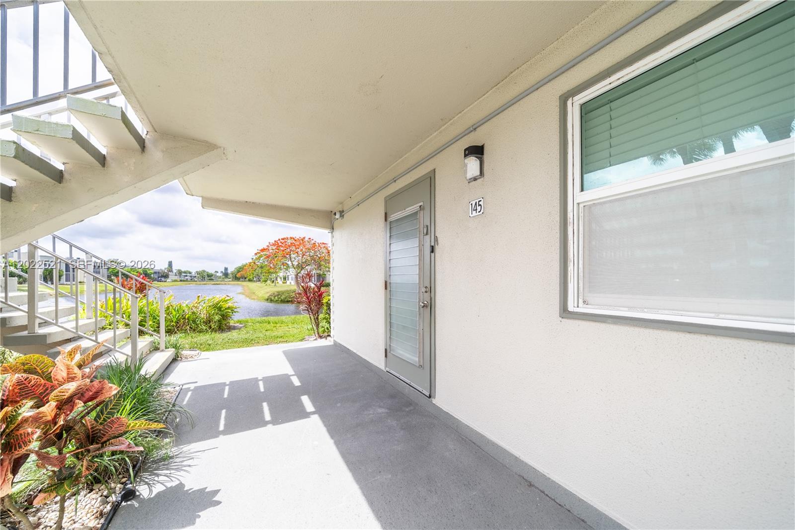 An exterior view of a ground-level apartment entrance with a patio and lake view — 145 Brittany D # 145, Delray Beach FL 33446, DELRAY BEACH, FL
