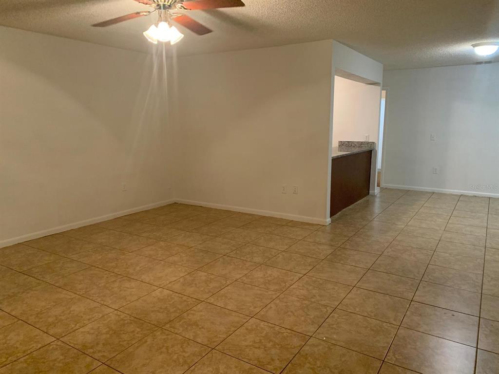 An empty room with tan tile flooring, a ceiling fan, and a kitchen pass-through — 858 FOX LAKE DRIVE UNIT 858, LAKELAND, FL