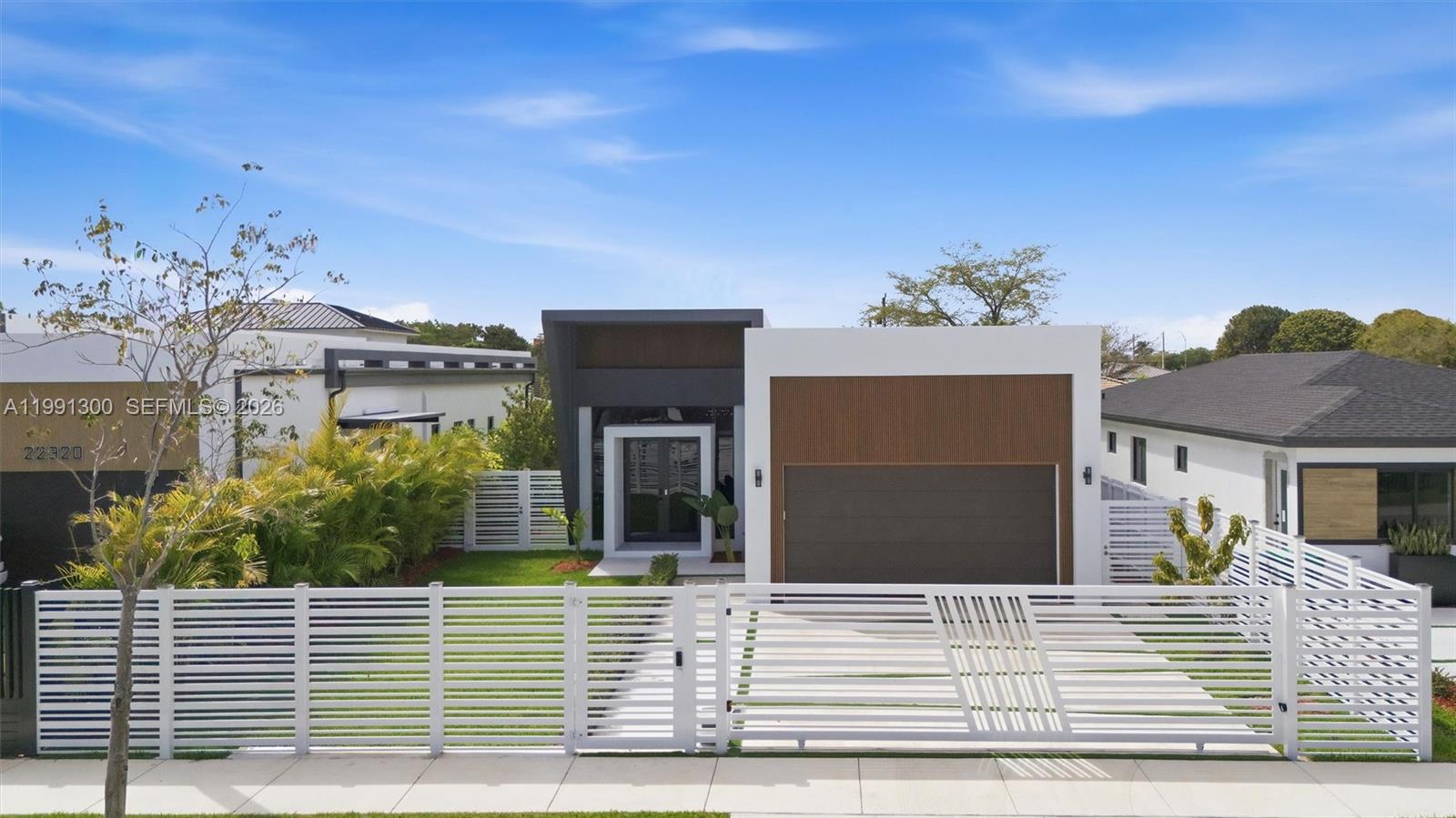 A modern single-story house features a white fence, a garage, and a dark entryway — 22900 SW 122 PL, Miami FL 33170, MIAMI, FL
