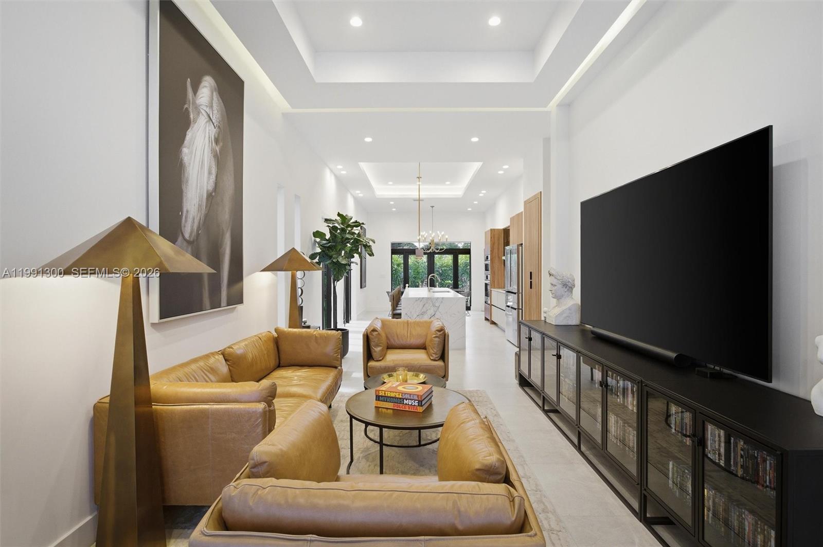 A modern living room with tan leather seating, a large television, and an open kitchen — 22900 SW 122 PL, Miami FL 33170, MIAMI, FL