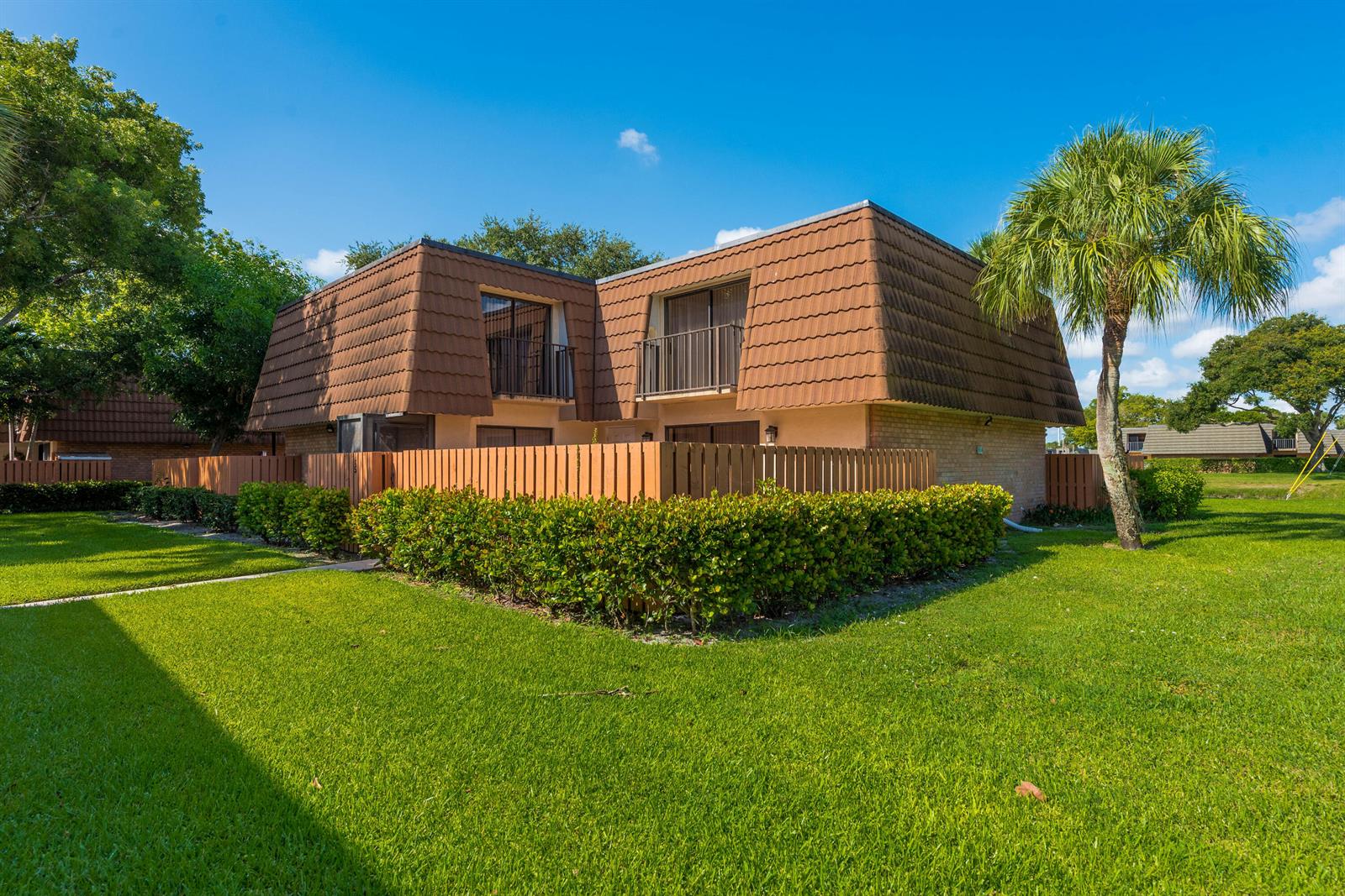 A two-story townhouse with a brown mansard roof, balconies, and a fenced-in patio area — 185 Charter Way, West Palm Beach FL 33407, WEST PALM BEACH, FL