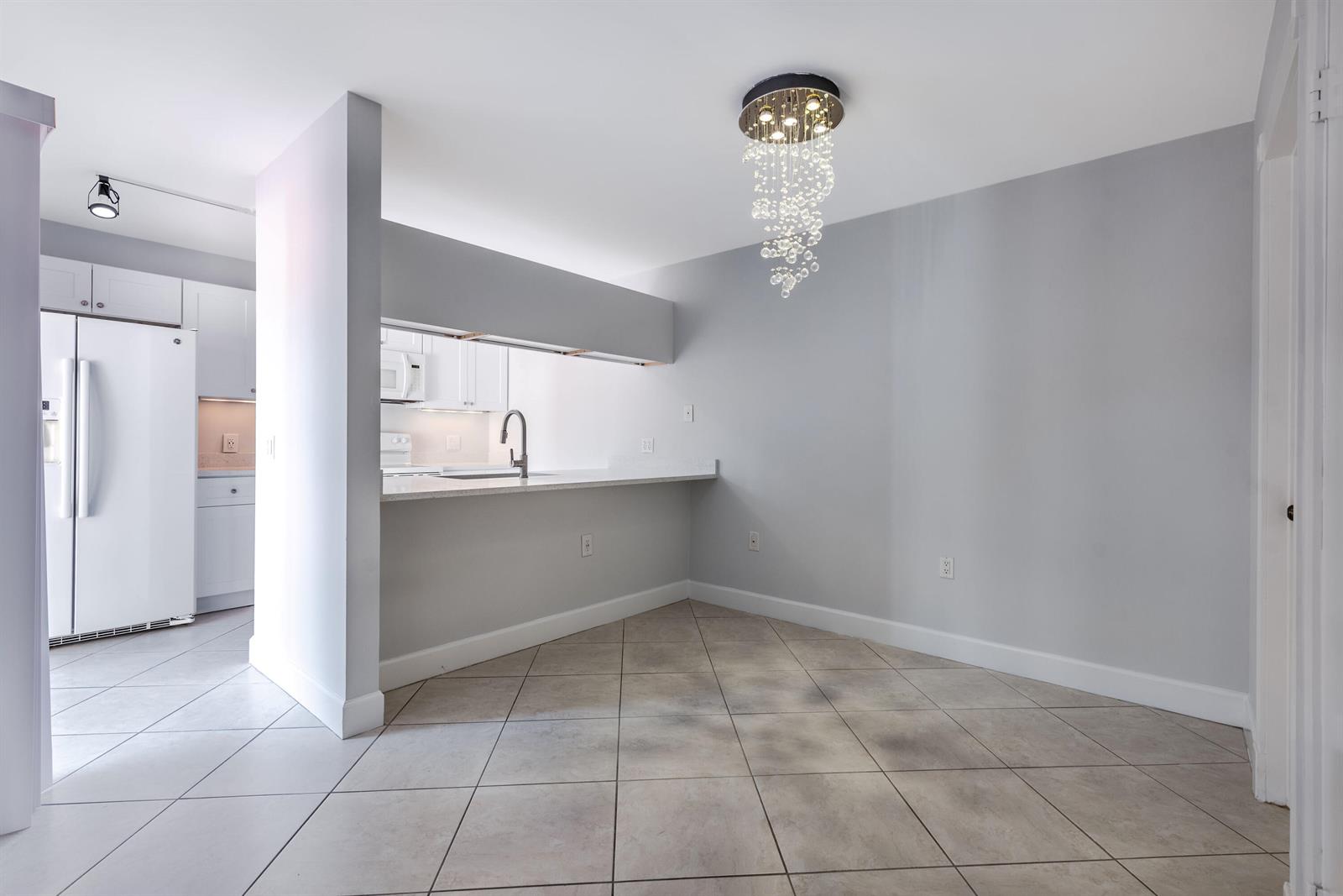 A dining area with tile flooring, a crystal chandelier, and a breakfast bar pass-through window — 185 Charter Way, West Palm Beach FL 33407, WEST PALM BEACH, FL