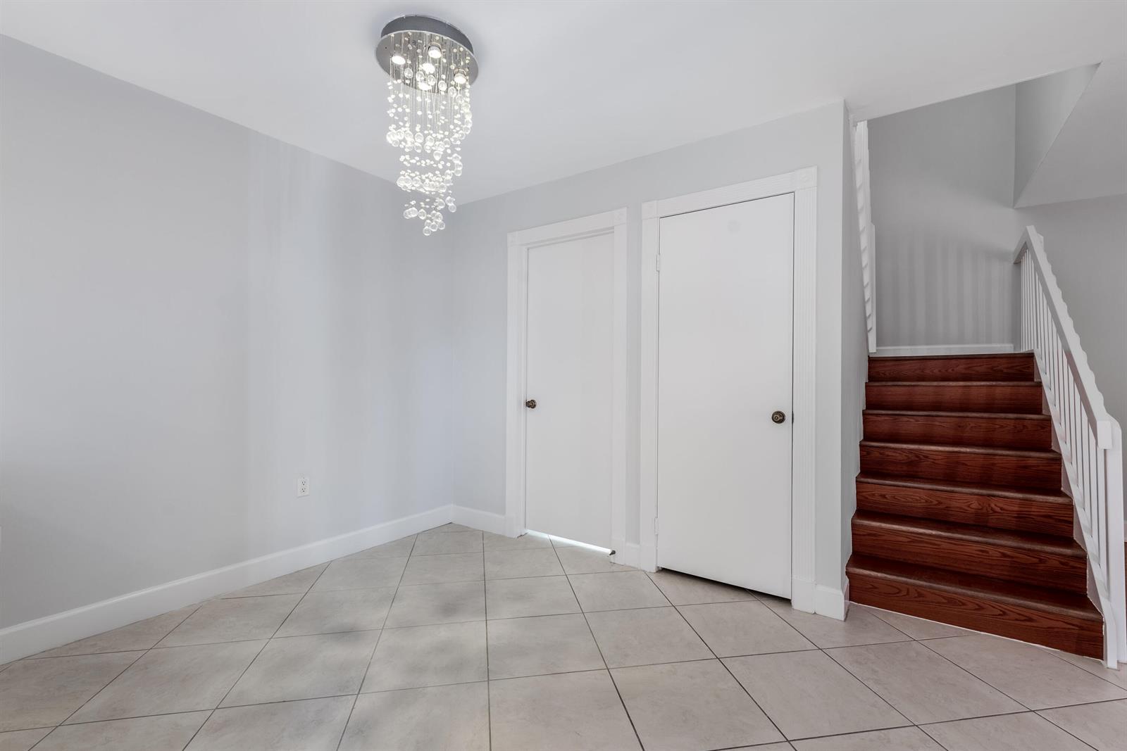 A foyer features light gray walls, tile flooring, a crystal chandelier, and a wooden staircase — 185 Charter Way, West Palm Beach FL 33407, WEST PALM BEACH, FL