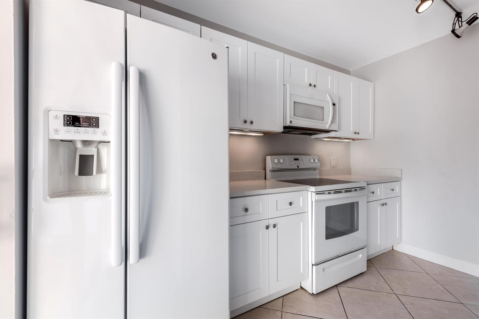 A white kitchen features a refrigerator, stove, microwave, and cabinetry with light-colored countertops — 185 Charter Way, West Palm Beach FL 33407, WEST PALM BEACH, FL