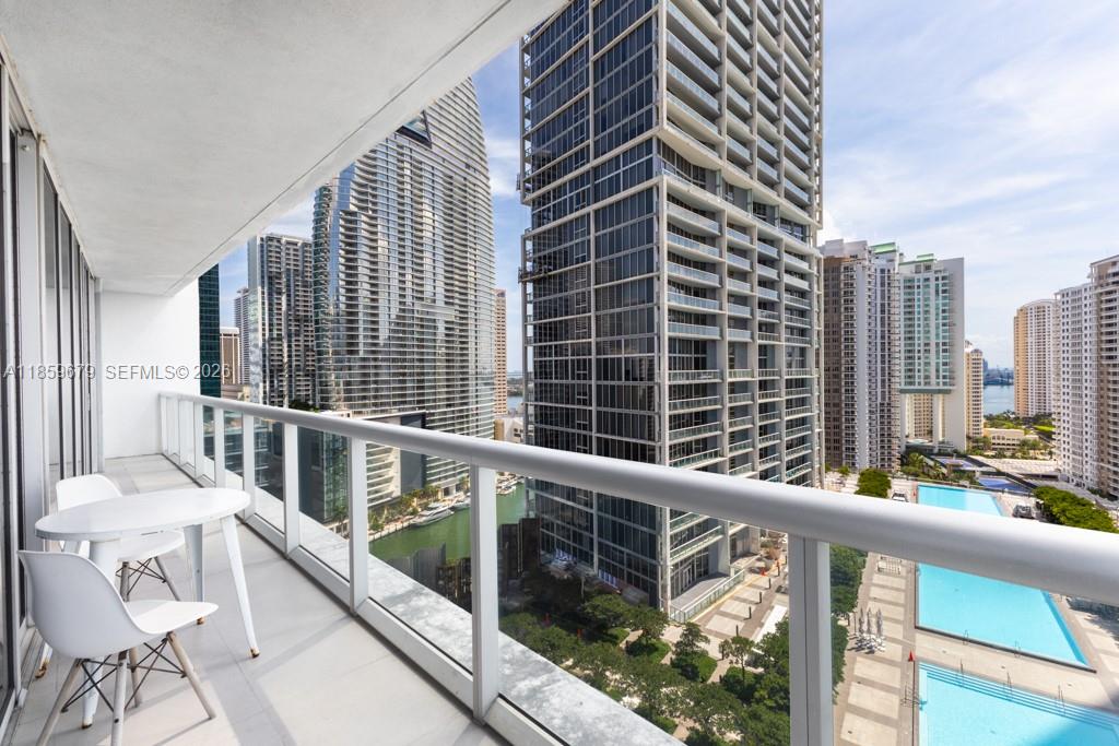 A balcony with a small table and chairs overlooks a city skyline and pools — 485 Brickell Ave # 2210, Miami FL 33131, MIAMI, FL