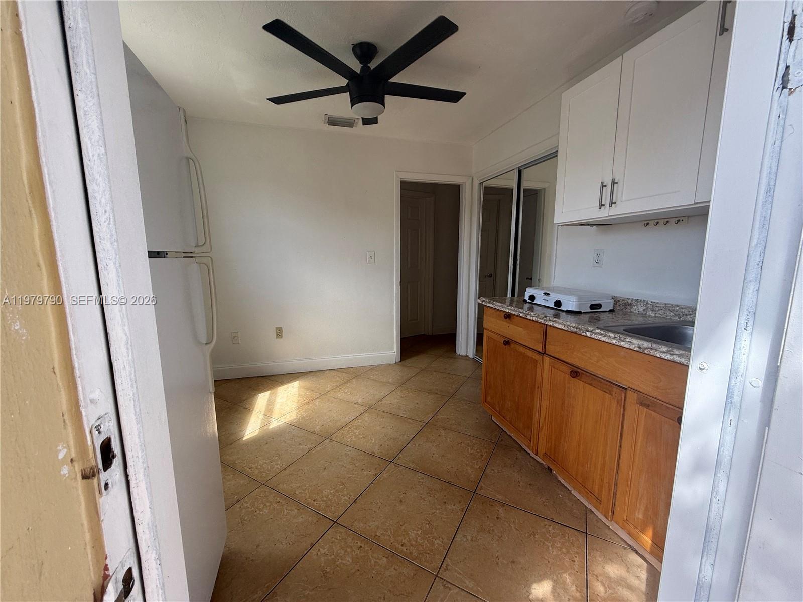 A small kitchen features white upper cabinets, wood lower cabinets, a refrigerator, and tiled flooring — 20221 SW 112th Ct # 2, Miami FL 33189, MIAMI, FL