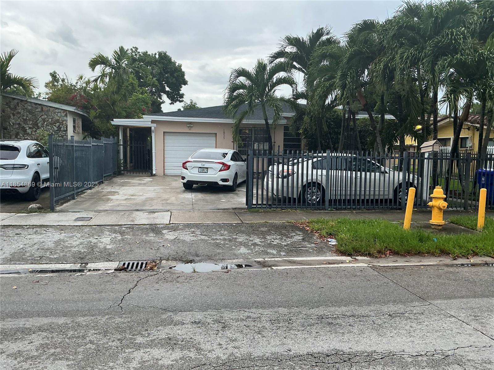 A single-story house with a white garage, fenced driveway, and palm trees in the front yard — 1855 NW 32nd St, Miami FL 33142, MIAMI, FL