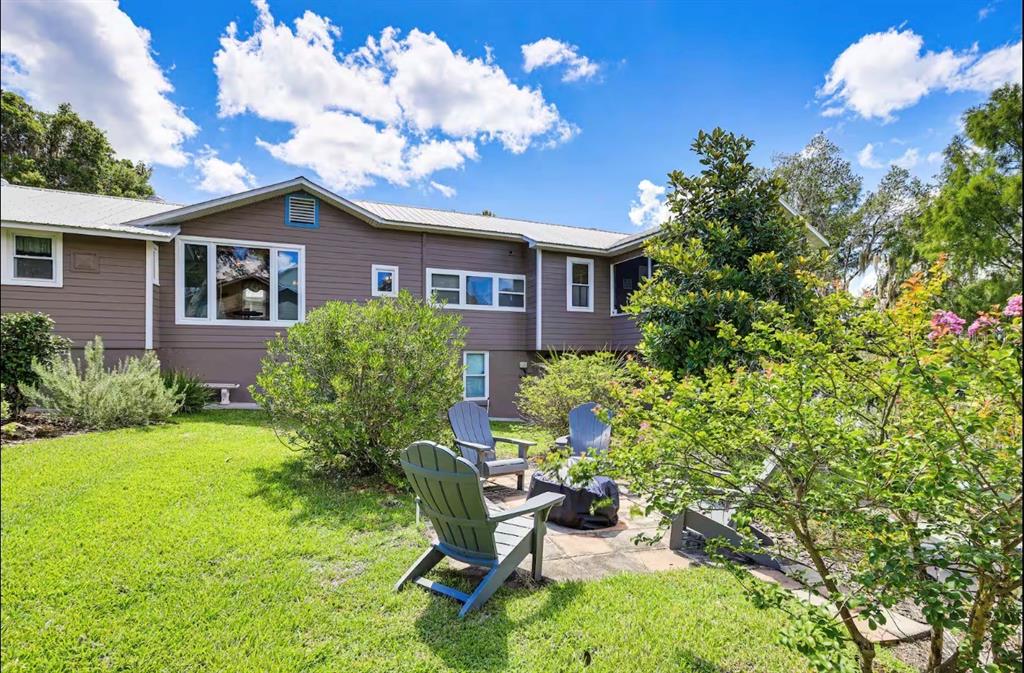 A brown house with a metal roof overlooks a backyard patio with Adirondack chairs — 20906 RIVER DRIVE, DUNNELLON, FL