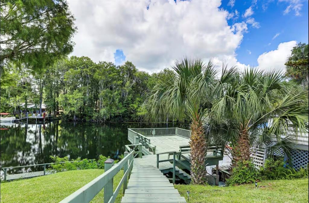 A wooden walkway leads to a deck overlooking a calm lake surrounded by lush trees — 20906 RIVER DRIVE, DUNNELLON, FL