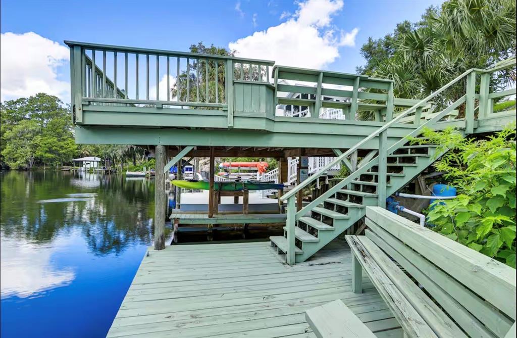 A wooden deck with stairs and a bench overlooks a calm river with kayaks stored underneath — 20906 RIVER DRIVE, DUNNELLON, FL