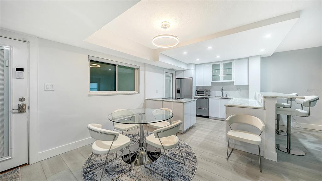 A modern kitchen and dining area features white cabinetry, stainless steel appliances, and tile flooring — 1150 TARPON CENTER DRIVE UNIT 1-C #103, VENICE, FL