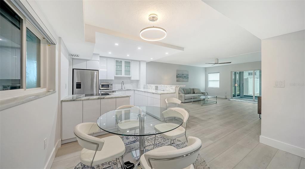 A modern open-concept kitchen and dining area with white cabinetry, marble countertops, and light flooring — 1150 TARPON CENTER DRIVE UNIT 1-C #103, VENICE, FL
