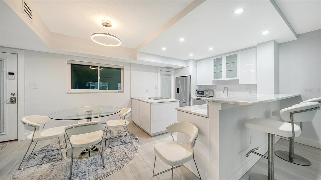 A modern kitchen and dining area featuring white cabinetry, a glass table, and bar seating — 1150 TARPON CENTER DRIVE UNIT 1-C #103, VENICE, FL