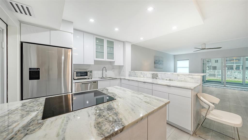 A modern kitchen features white cabinetry, marble countertops, a center island, and stainless steel appliances — 1150 TARPON CENTER DRIVE UNIT 1-C #103, VENICE, FL