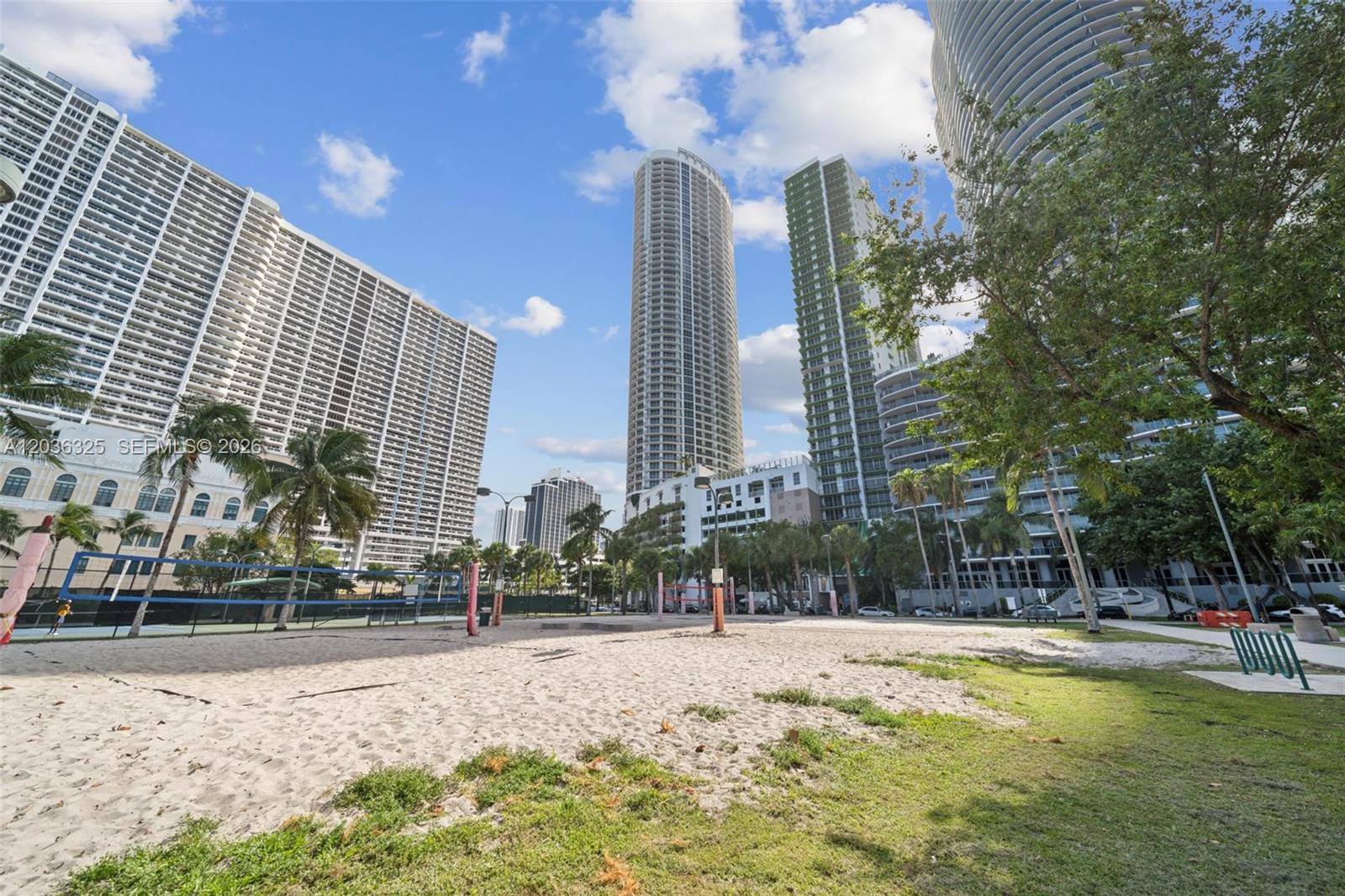 A sandy volleyball court sits in front of several tall residential skyscrapers under a blue sky — 1750 N Bayshore Dr # 4315, Miami FL 33132, MIAMI, FL
