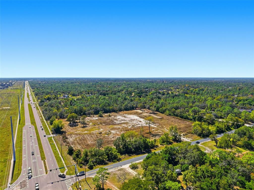 An aerial view shows a large, cleared vacant lot bordered by a highway and trees — 9247 SUNSHINE GROVE ROAD, BROOKSVILLE, FL