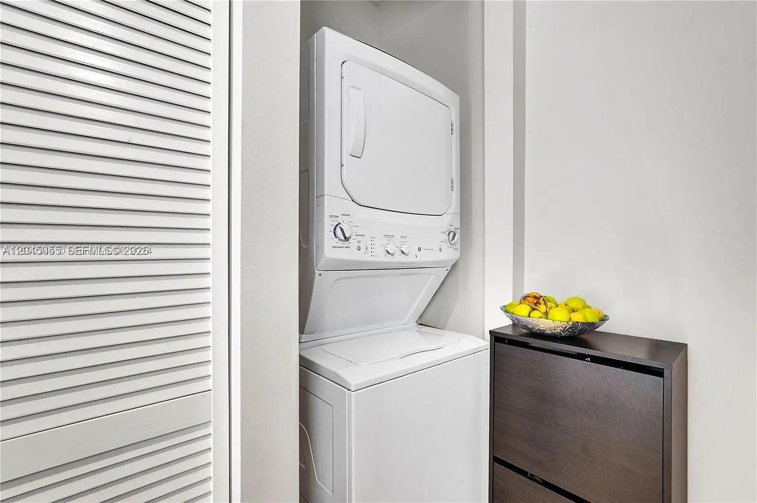 A stacked washer and dryer unit sits in a closet next to a storage cabinet — 6319 NW 105 CT # 0, Doral FL 33178, DORAL, FL
