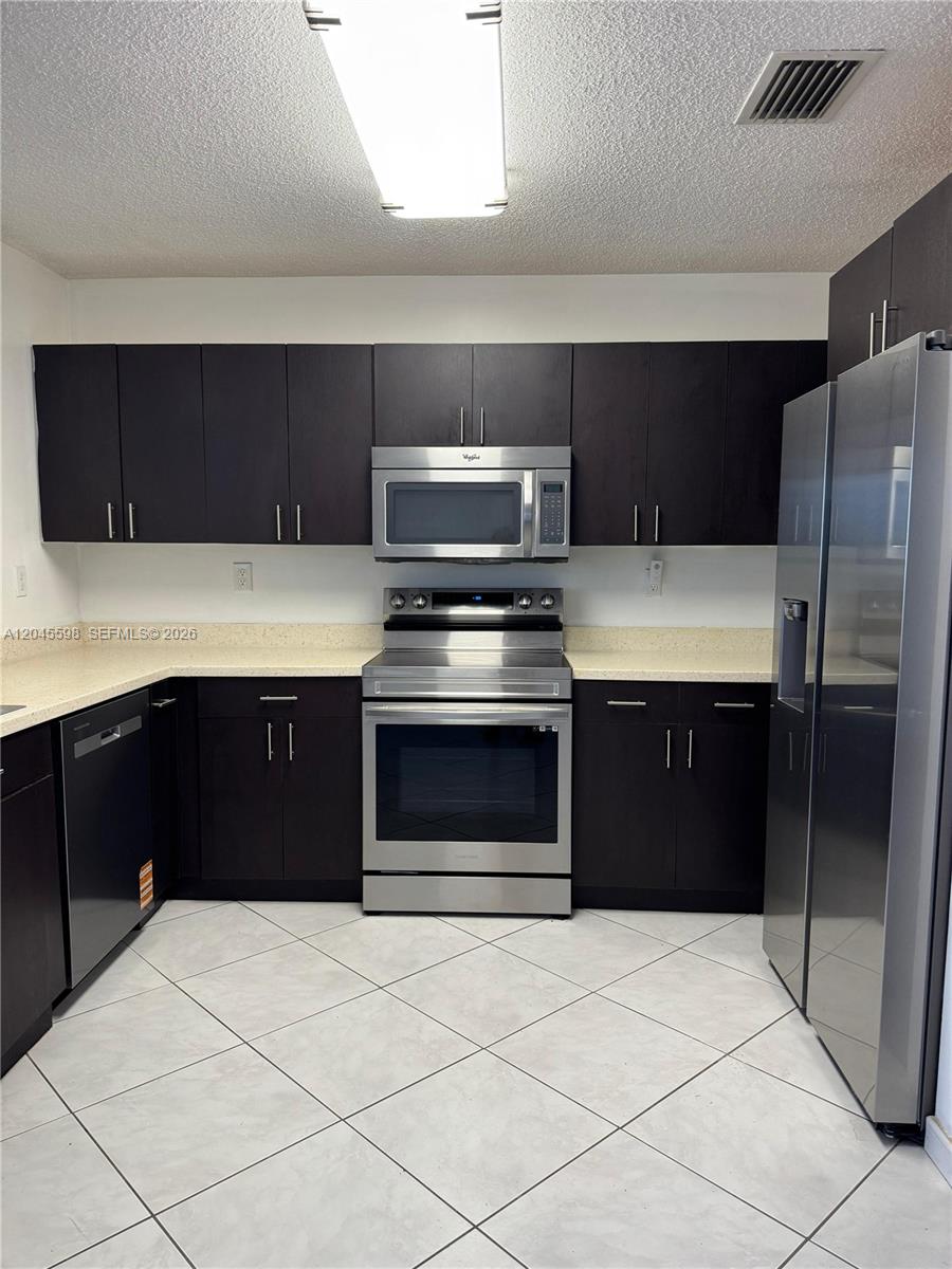 A kitchen features dark wood cabinets, stainless steel appliances, and light-colored countertops and tile flooring — 13907 SW 177th St # 13907, Miami FL 33177, MIAMI, FL