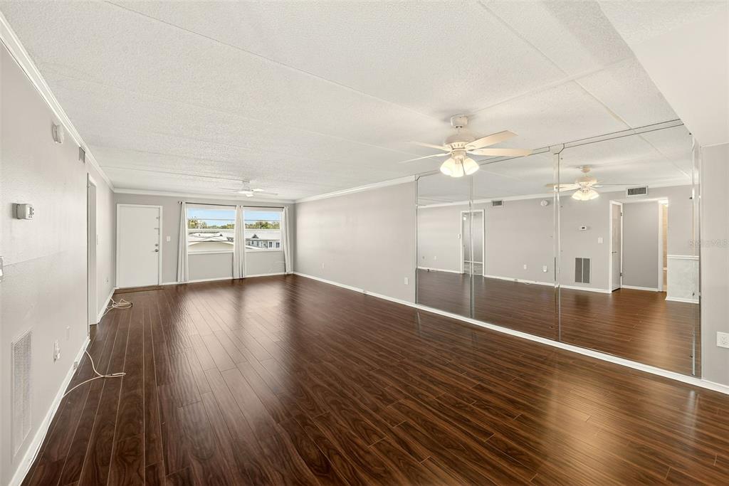 A spacious living room with dark wood flooring, white walls, and a large mirrored wall — 12300 PARK BOULEVARD UNIT 116, SEMINOLE, FL