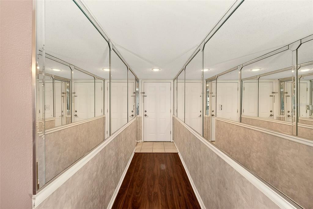 A narrow hallway features wood-look flooring, beige textured walls, and large wall-to-wall mirrors — 12300 PARK BOULEVARD UNIT 116, SEMINOLE, FL