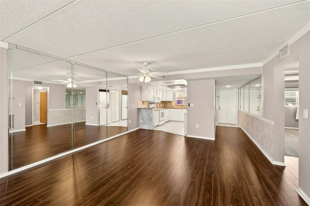 A living room with wood-look flooring, mirrored walls, and an open view into the kitchen — 12300 PARK BOULEVARD UNIT 116, SEMINOLE, FL