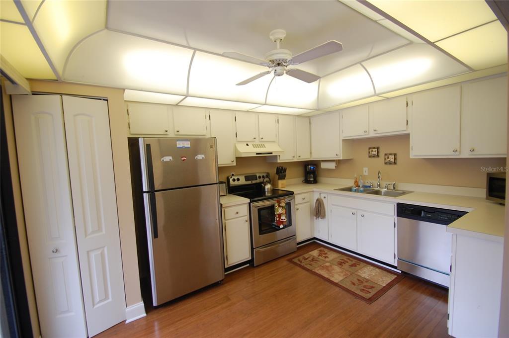 A kitchen with white cabinets, stainless steel appliances, wood flooring, and a tray ceiling — 1637 BROOKHOUSE COURT UNIT BR243, SARASOTA, FL